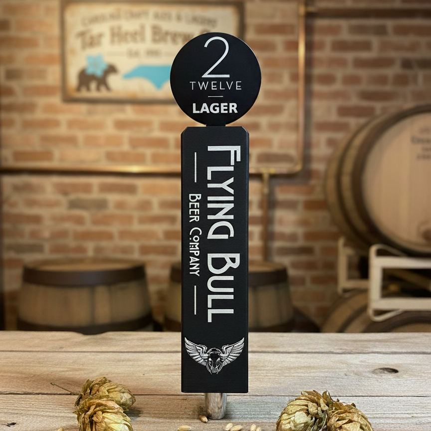 Flying Bull Beer Company tap handle with hops on a wooden surface against a brick wall.